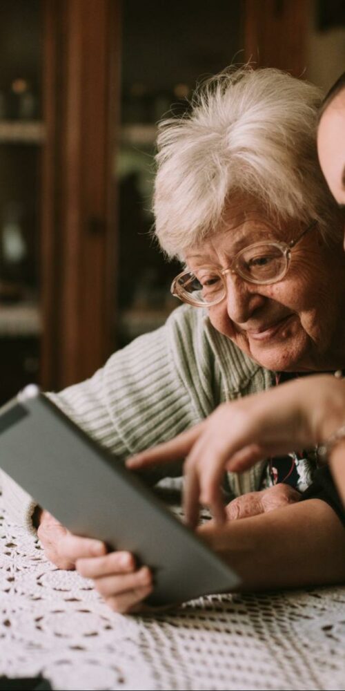 Grandmother and granddaughter sitting at a table and looking at a tablet together.