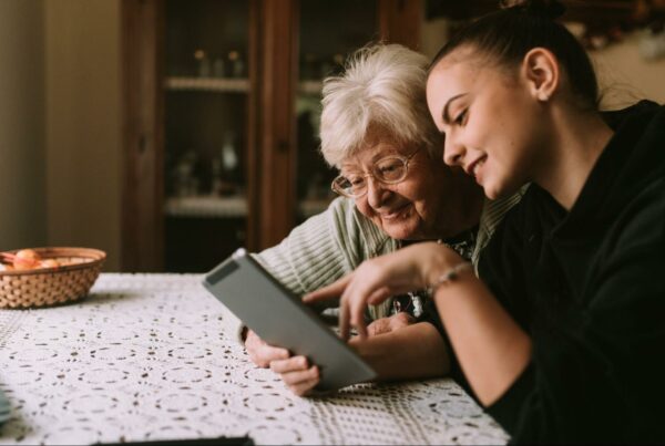 Grandmother and granddaughter sitting at a table and looking at a tablet together.