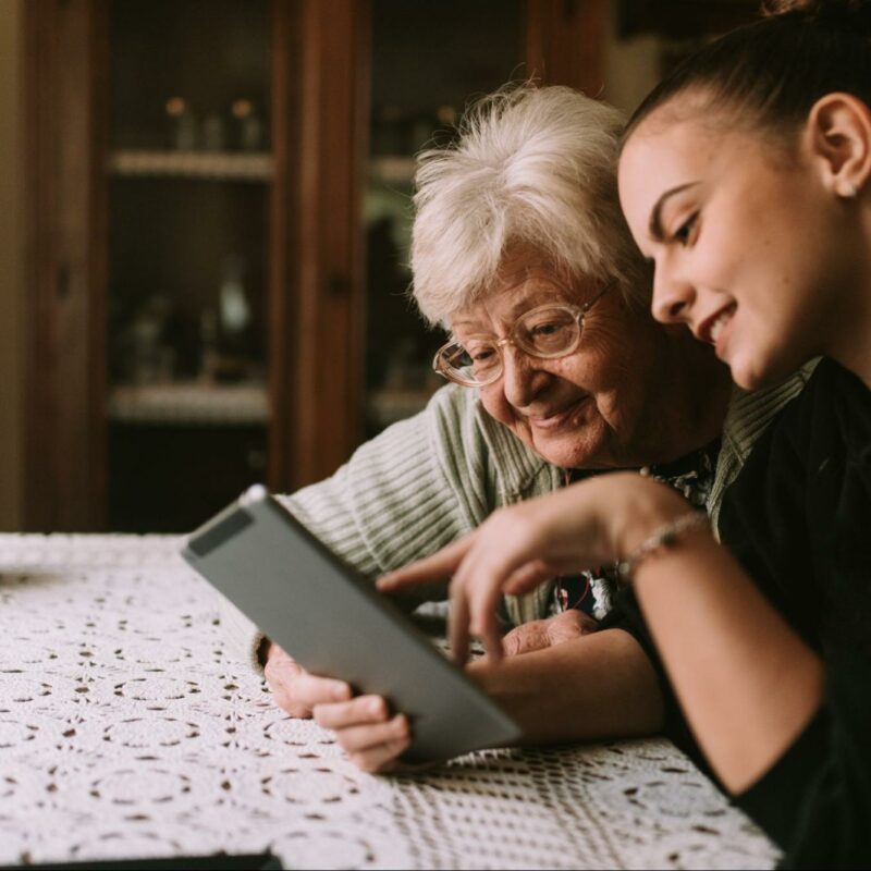 Grandmother and granddaughter sitting at a table and looking at a tablet together.